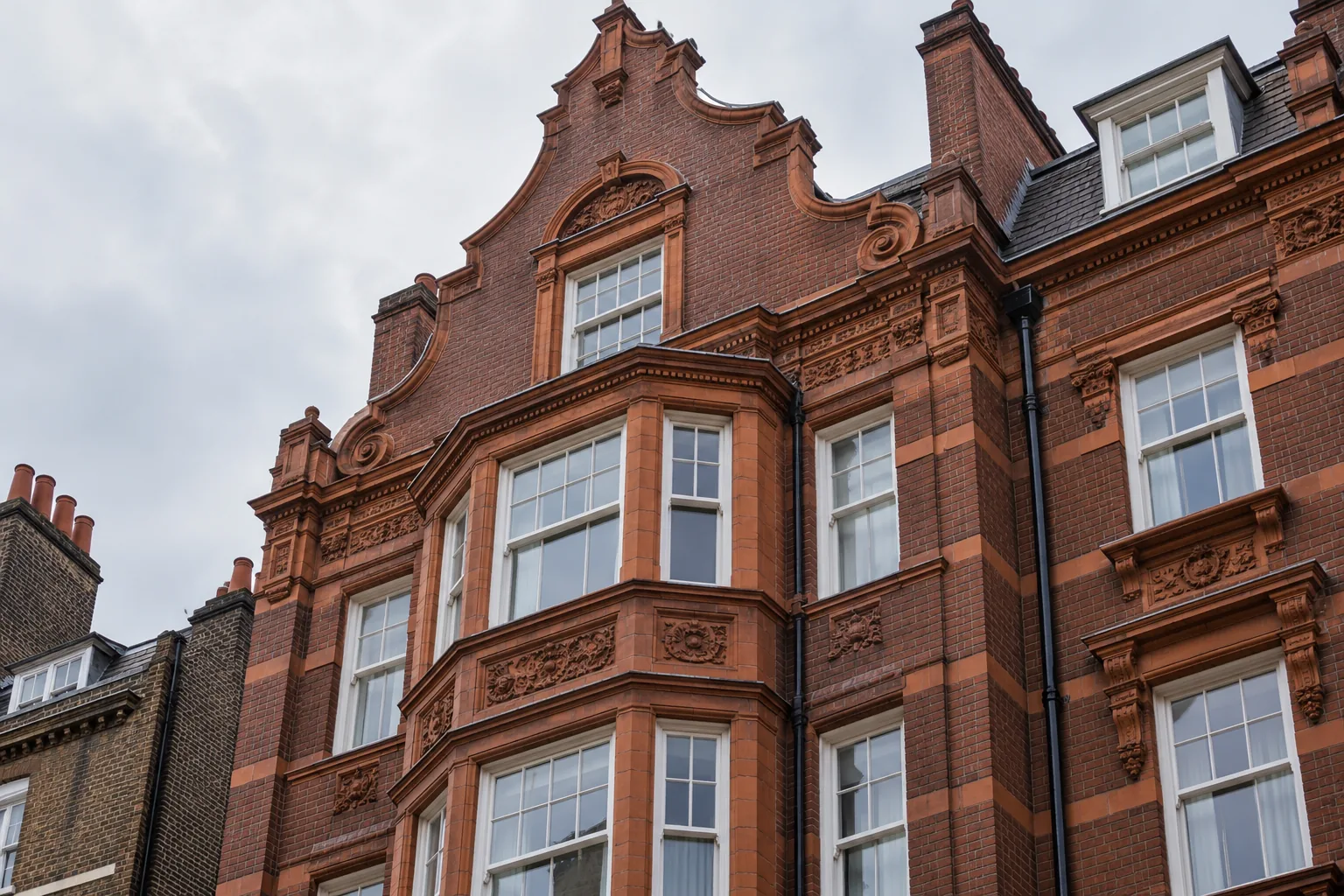 Red-brick facade with a curved Dutch gable, ornamental terracotta bays and white sash windows