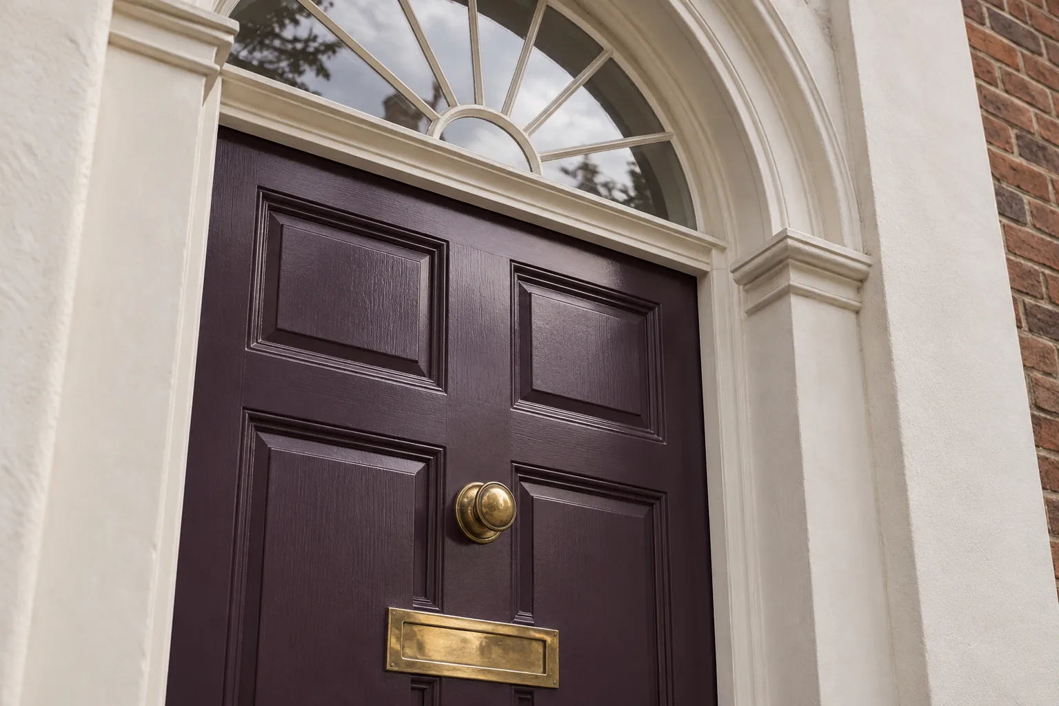 Close view of plum-painted door mouldings, a brass knob and letterplate beneath a fanlight
